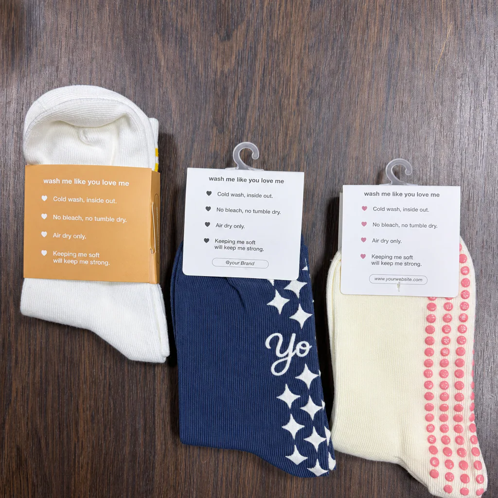 Factory-photographed physical Pilates grip sock packaging samples showing a paper sleeve and hanging header cards